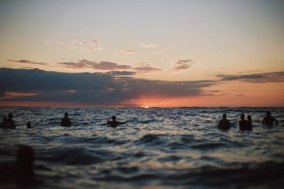 Swimmers in the ocean beneath a sunset sky