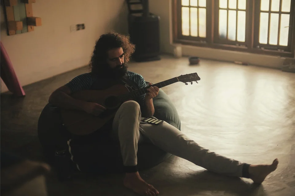 A musician seated on a tiled floor with a guitar