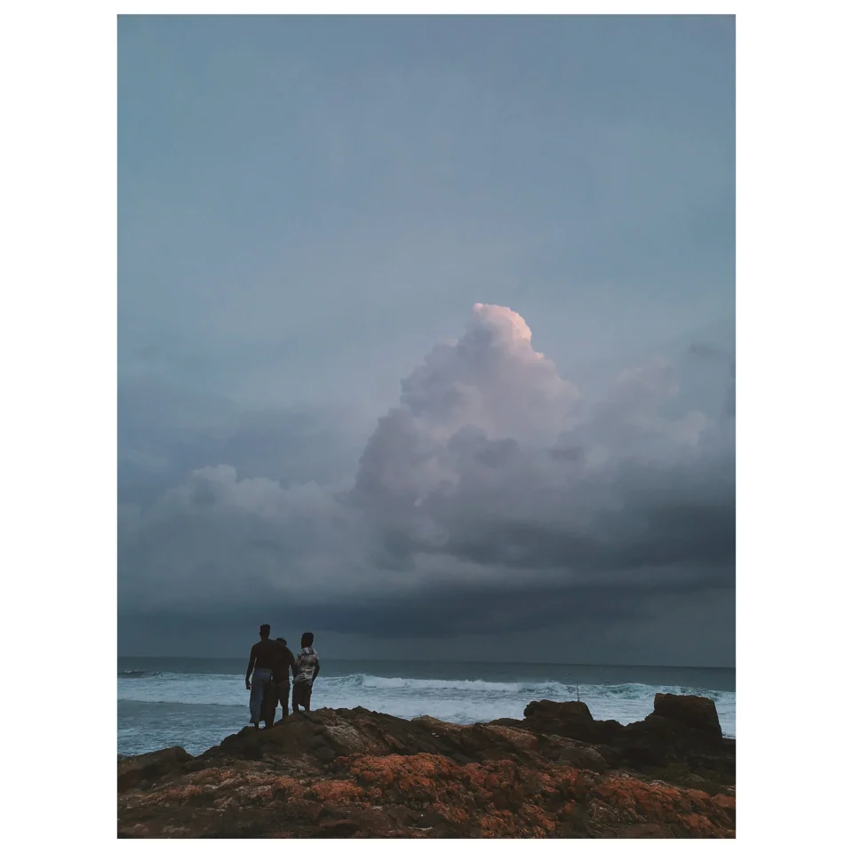 Two figures on rocks beneath a cloud-filled coastal sky