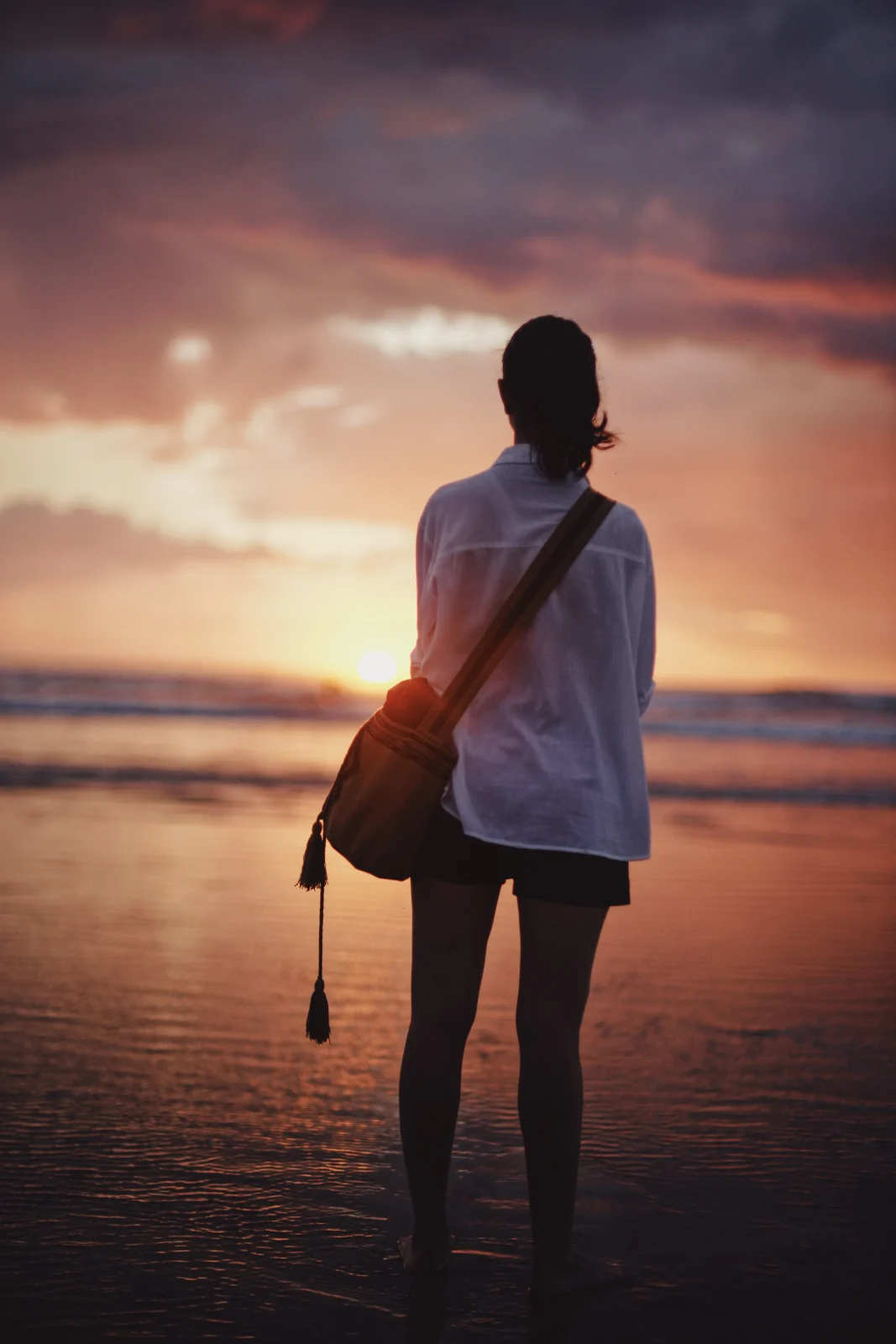 A person standing at the shoreline at sunset