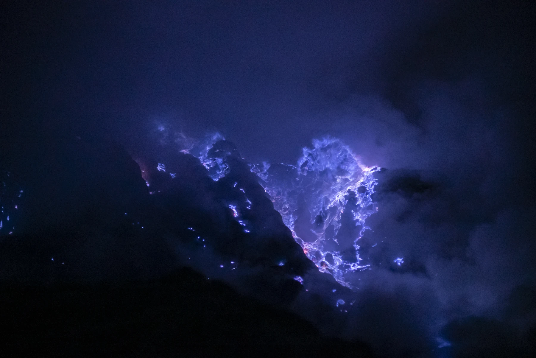 Blue volcanic flames illuminating dark rock and rising smoke