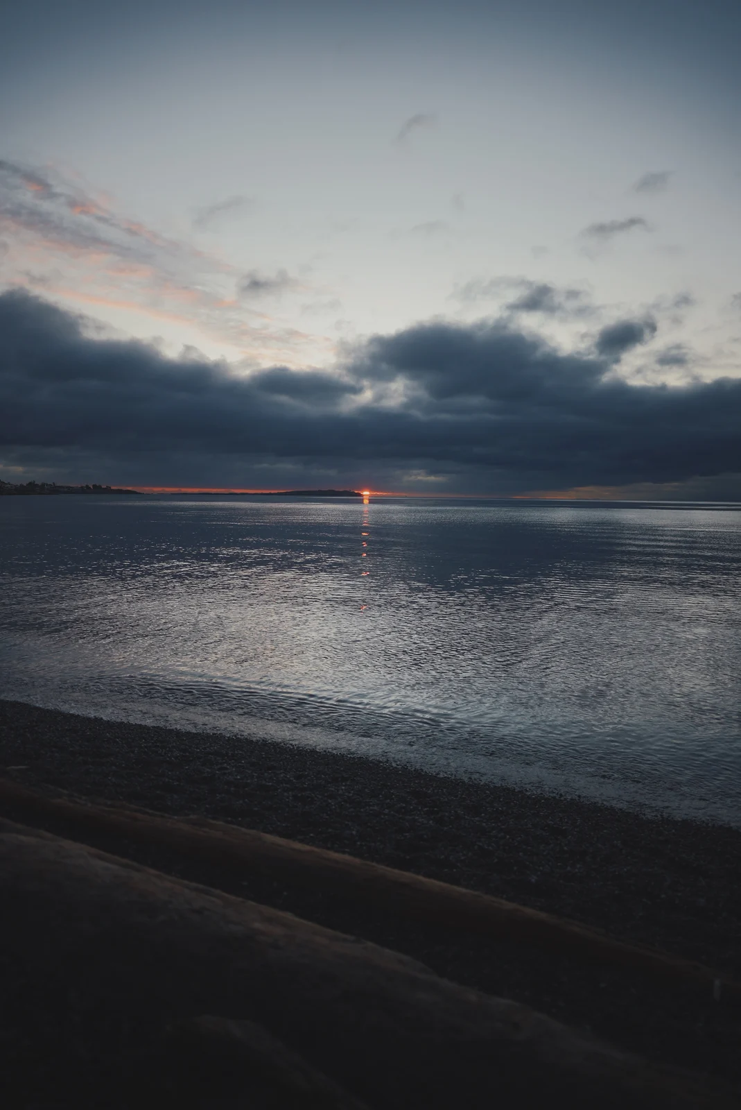 A small setting sun over calm grey water