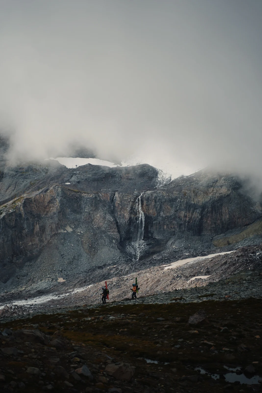 Two skiers beneath a misty cliff and waterfall