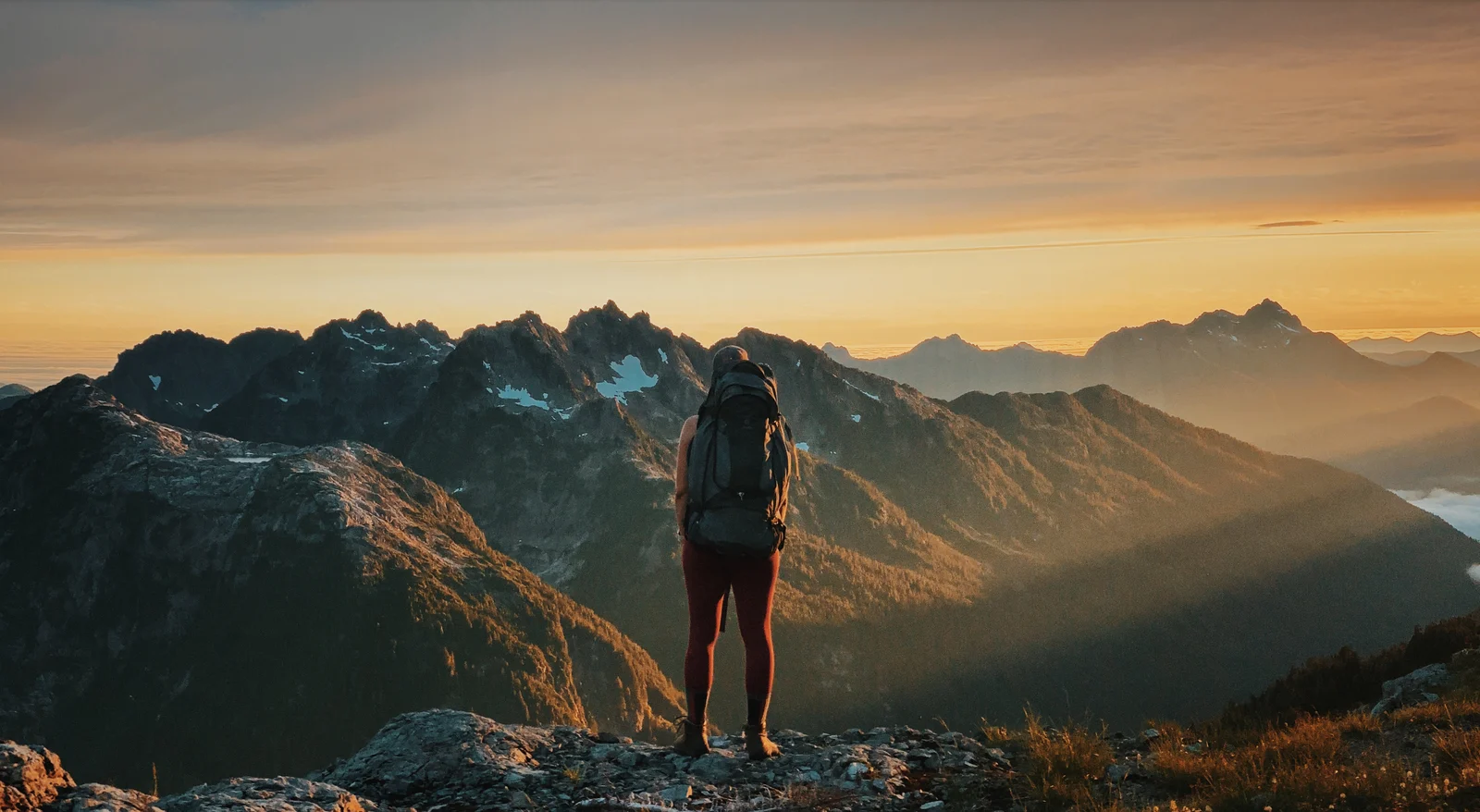A backpacker overlooking mountain ridges at golden hour