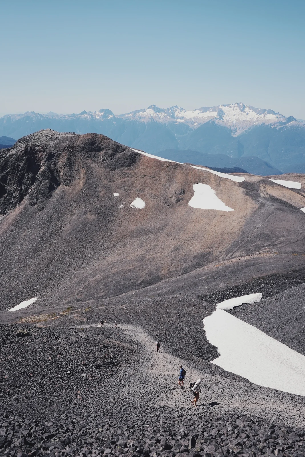 Hikers descending a volcanic valley past patches of snow
