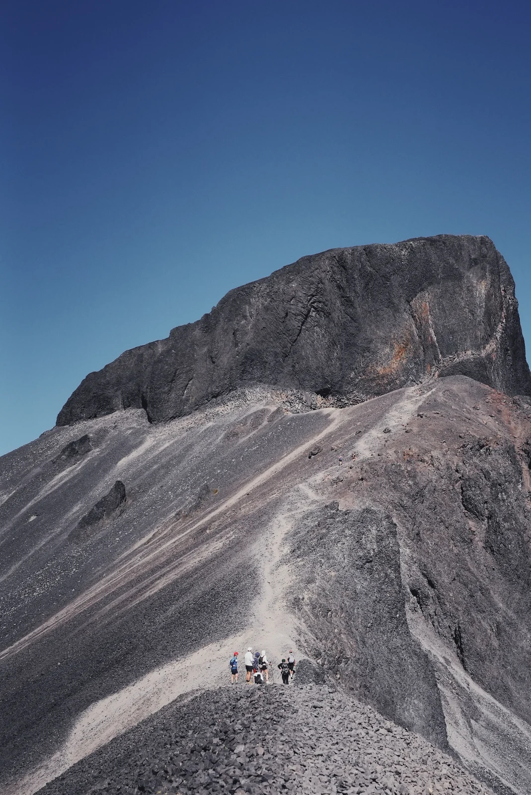Hikers beneath a towering volcanic rock face