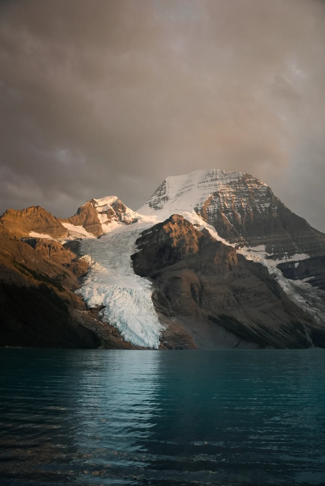 A glacier above a turquoise lake and sunlit peaks